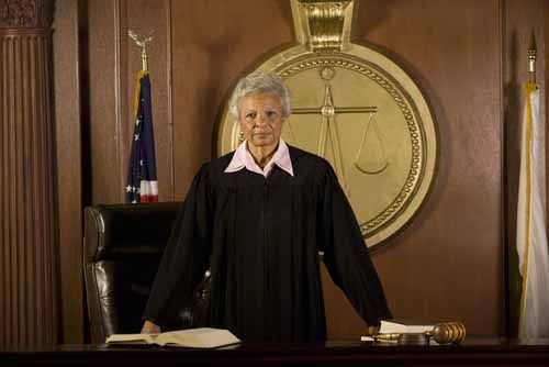 A judge stands at her desk in a courtroom